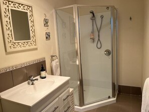 A bathroom with a glass-enclosed shower, a sink with a mirror, and a decorative wall panel.
