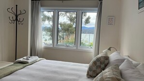 Un dormitorio con cama, ventana con vistas a árboles y montañas, perchero y lámpara.