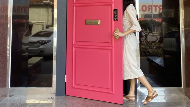 Una persona abre una puerta rosa brillante con un pomo de latón y una cerradura.