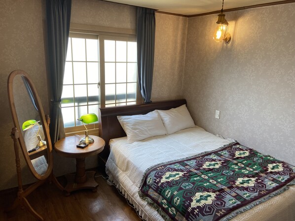 Un dormitorio con una cama, una mesita de noche, una lámpara, un espejo y una ventana con cortinas.