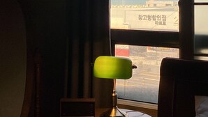 Habitación de hotel con vista a la costa, una mesita redonda con lámpara y una cama.