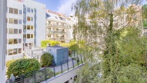 En flereetagers boligbygning med altaner, en tagterrasse og grøn bevoksning omkring.