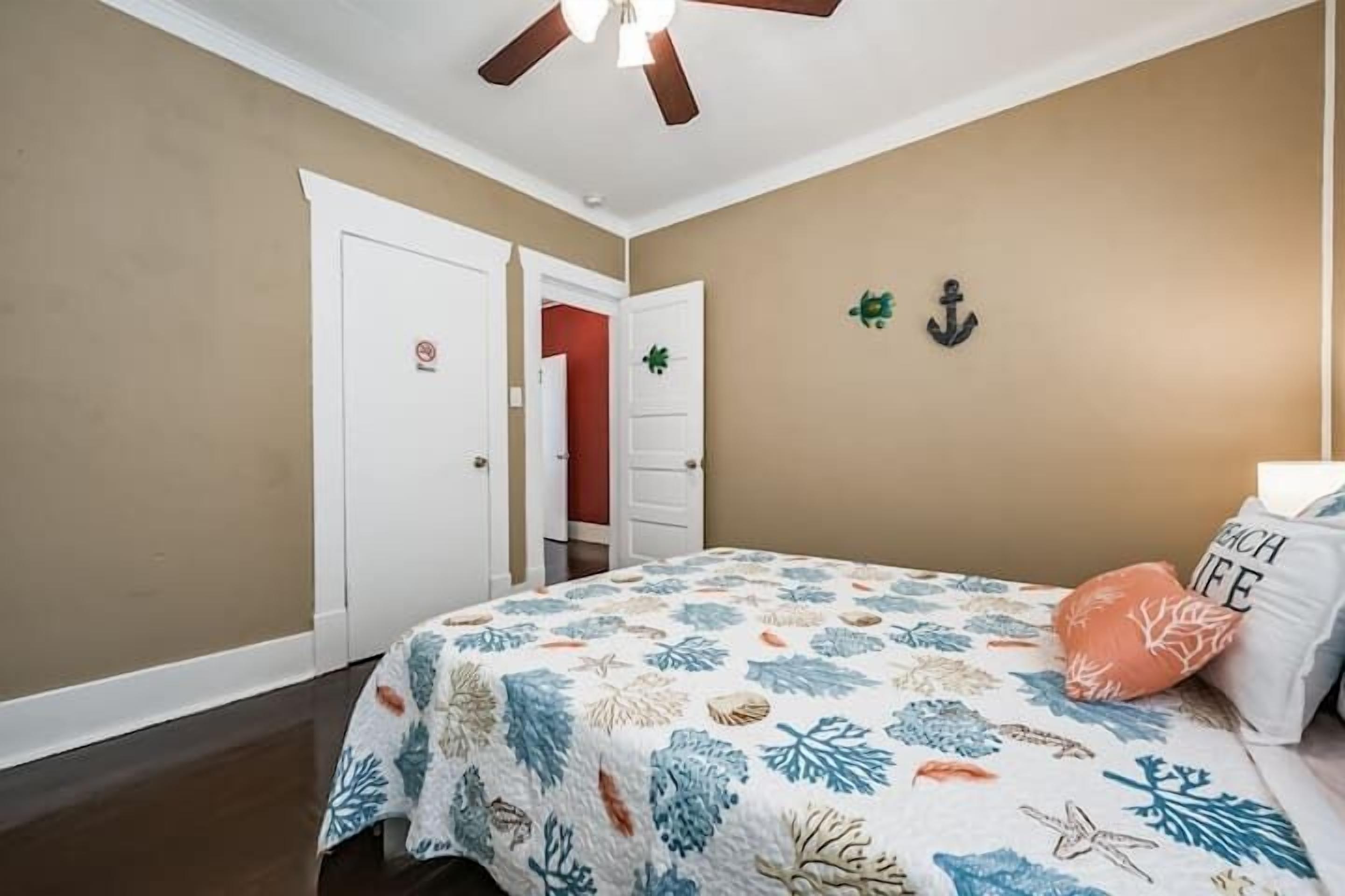 A bedroom with a bed, a ceiling fan, a door, and a wall with an anchor decoration.