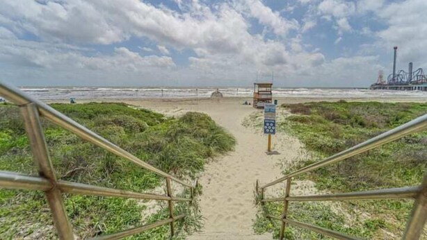 Un sendero de arena que lleva a una torre de salvavidas con un cartel, rodeado de arena y vegetación.