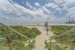 Een strandpad dat leidt naar een redershut met een bord, omgeven door zand en begroeiing.
