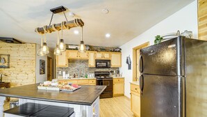 A kitchen with wooden cabinets, a stainless steel refrigerator, a central island with a black countertop, and a hanging light fixture.
