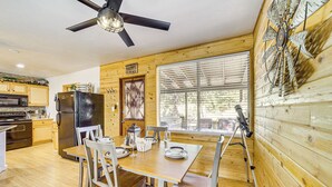 A wooden interior with a dining table set for four, a ceiling fan, and a large window with blinds.
