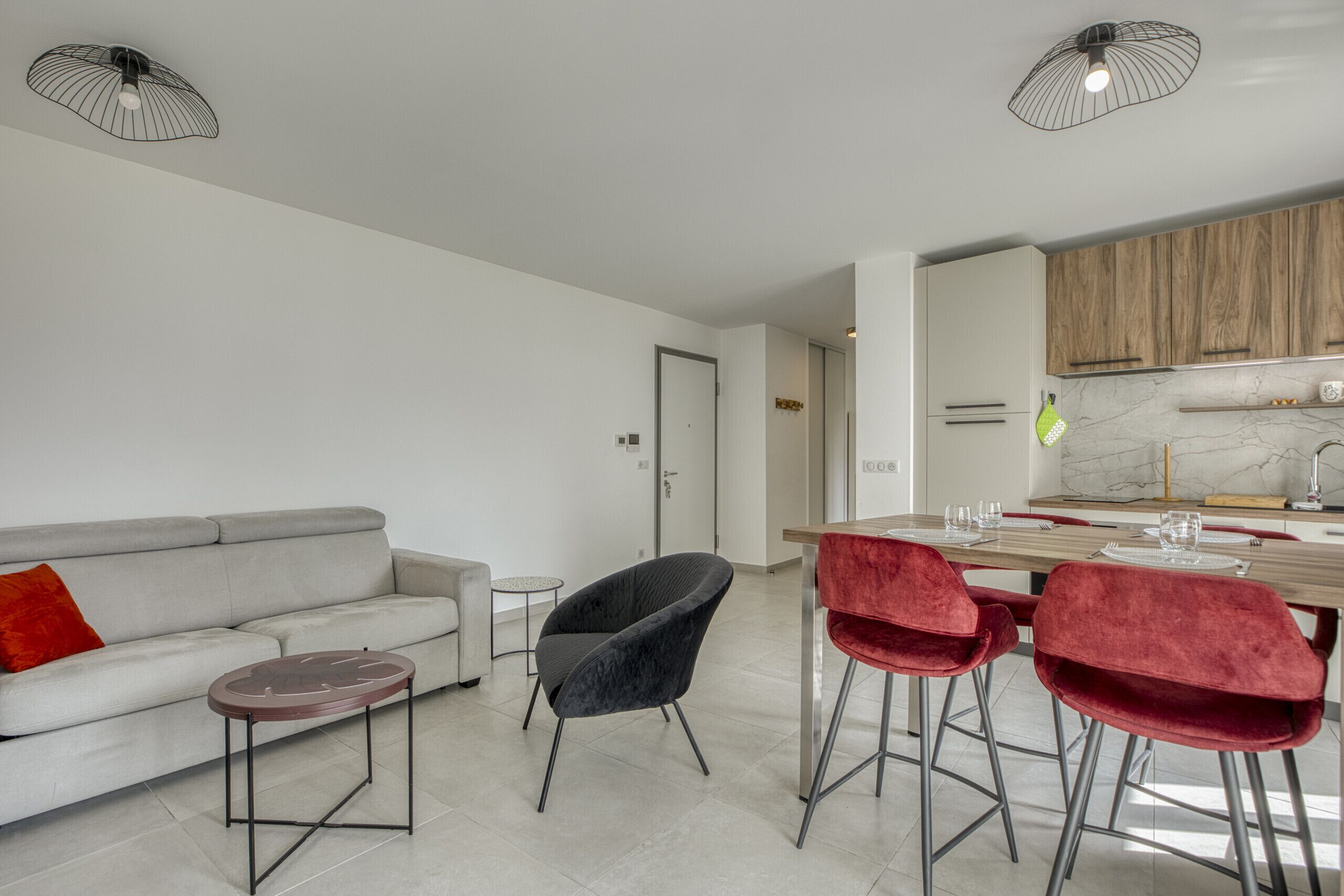 Una sala de estar moderna con un sofá, una mesa redonda de centro, una silla negra y un comedor con una mesa de madera y sillas rojas.