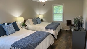 Ein Schlafzimmer mit zwei Betten, einem Deckenventilator, einem Fenster mit Jalousien, einem Schreibtisch mit Computer und einem Stuhl.