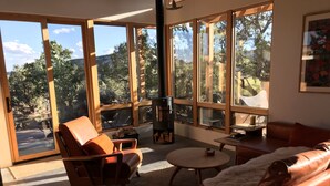 A spacious living room with large windows, a fireplace, leather furniture, and a cozy rug.