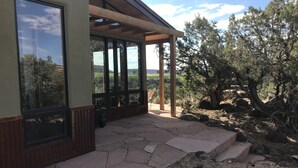 A covered patio with stone flooring, large windows, and a view of the surrounding landscape.