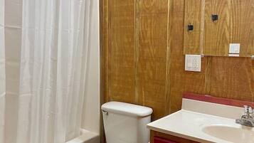 A bathroom with a wooden wall, a white toilet, a red cabinet, and a white sink.