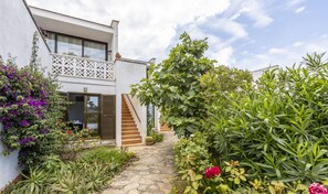 Une maison moderne avec un chemin en pierre, une végétation luxuriante et un balcon blanc.