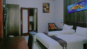 A hotel room with a bed, a chair, a desk, and a painting on the wall.