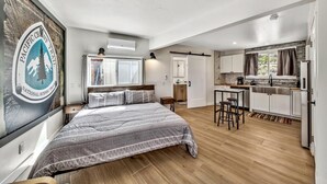 Une chambre avec un grand lit, un petit bureau et un coin cuisine.