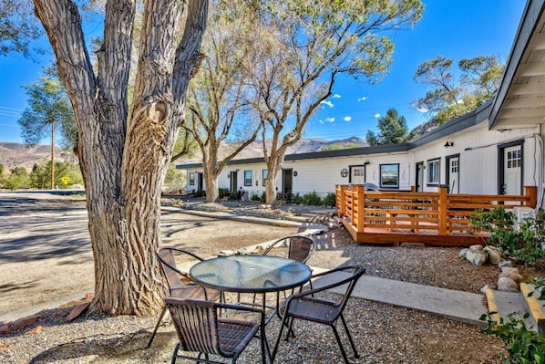 A rustic outdoor seating area with a table and chairs, surrounded by trees and a wooden fence.