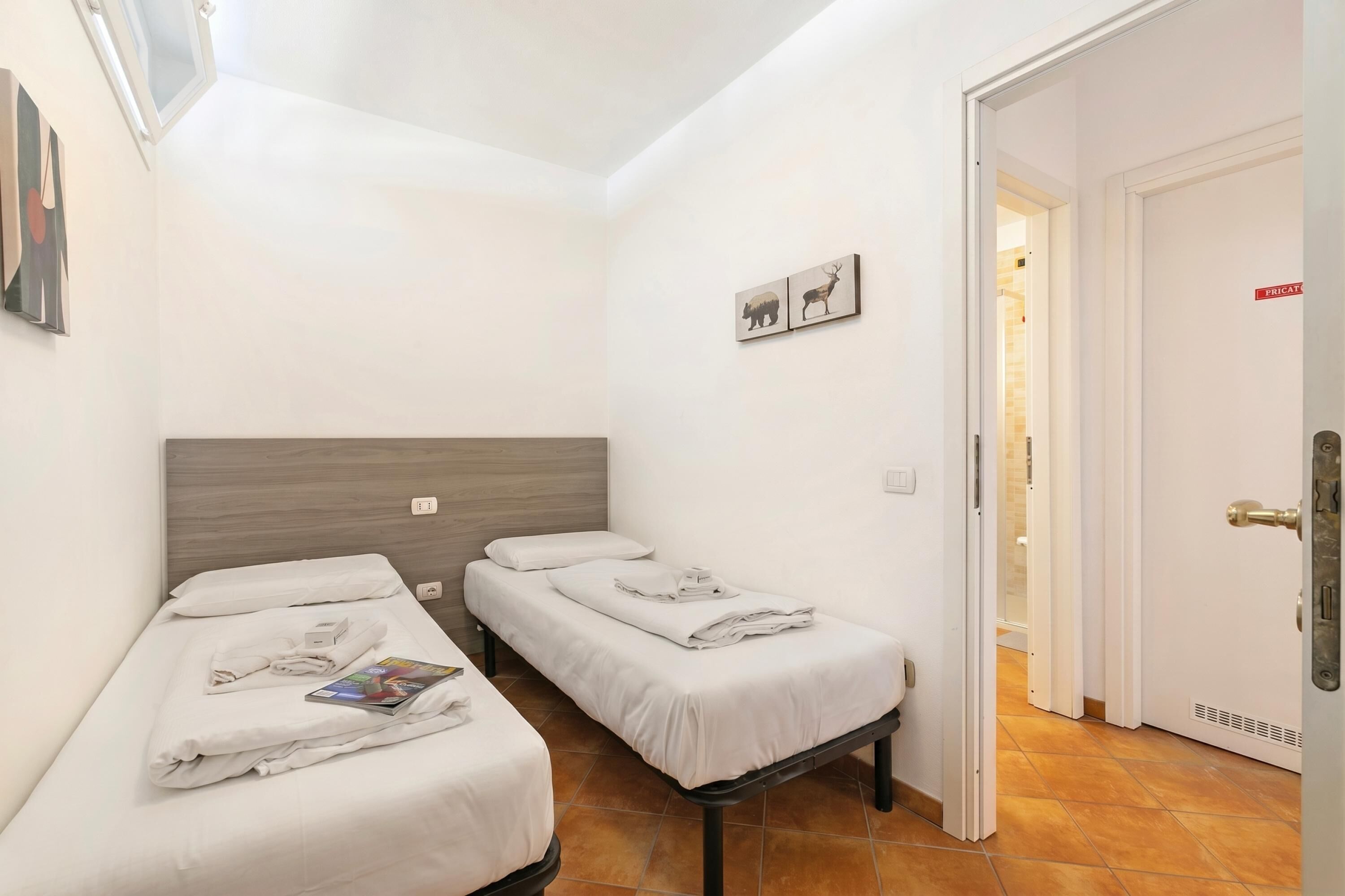 A small, clean room with two single beds, a wooden headboard, a door with a sign, and a wall-mounted picture.