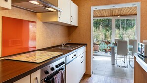 Una cocina moderna con armarios blancos, una campana extractora de acero inoxidable y un amplio ventanal con vistas a un balcón con mobiliario exterior.