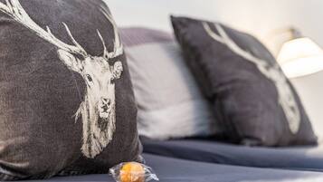 A bed with two pillows featuring a deer design, a small orange object on the bed, and a lamp in the background.