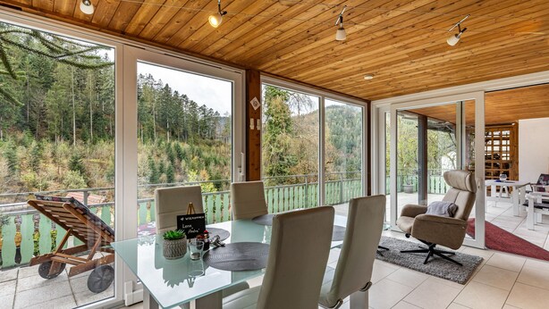 Un interior moderno con una mesa de vidrio, sillas y vistas a un área boscosa.