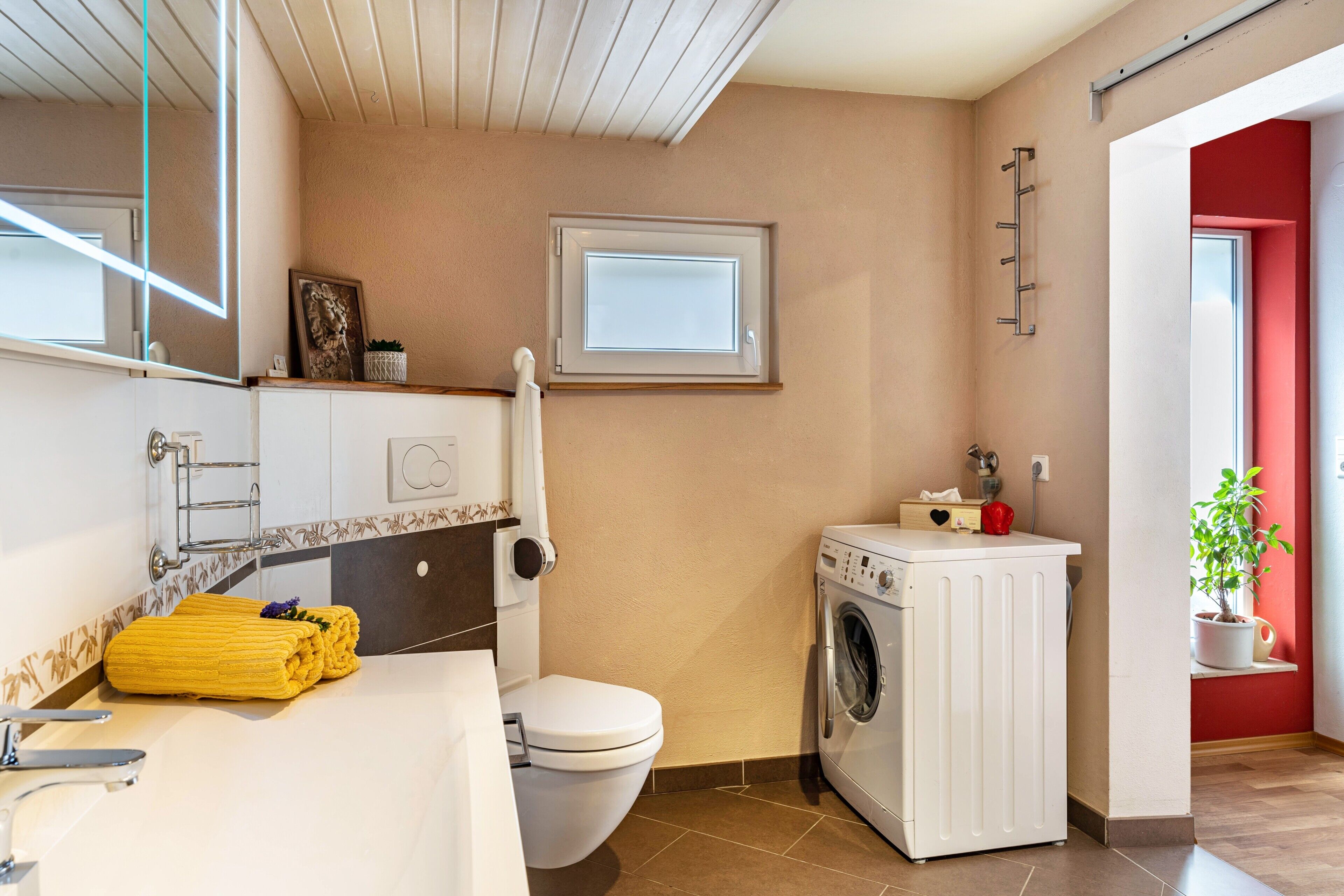 Une salle de bain équipée de toilettes, d’un lave-linge et d’un porte-serviettes.