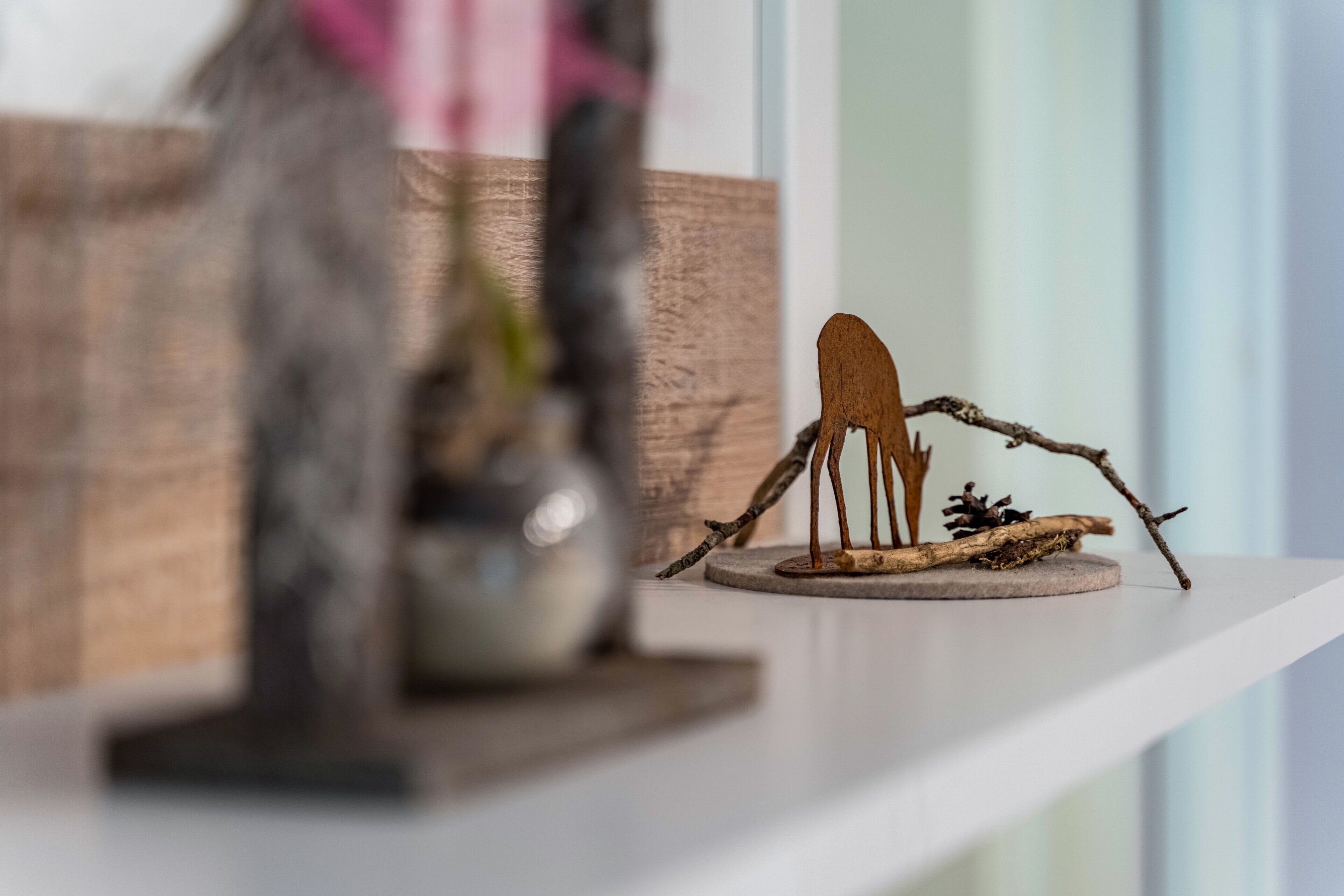 Eine kleine Vogel-Skulptur aus Holz auf einer runden Basis, platziert auf einem weißen Regal.