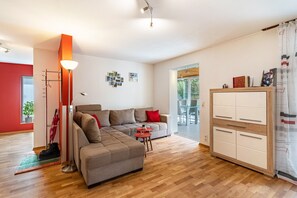 Un salon moderne avec un canapé d’angle, une petite table, un meuble et une vue sur l’extérieur.