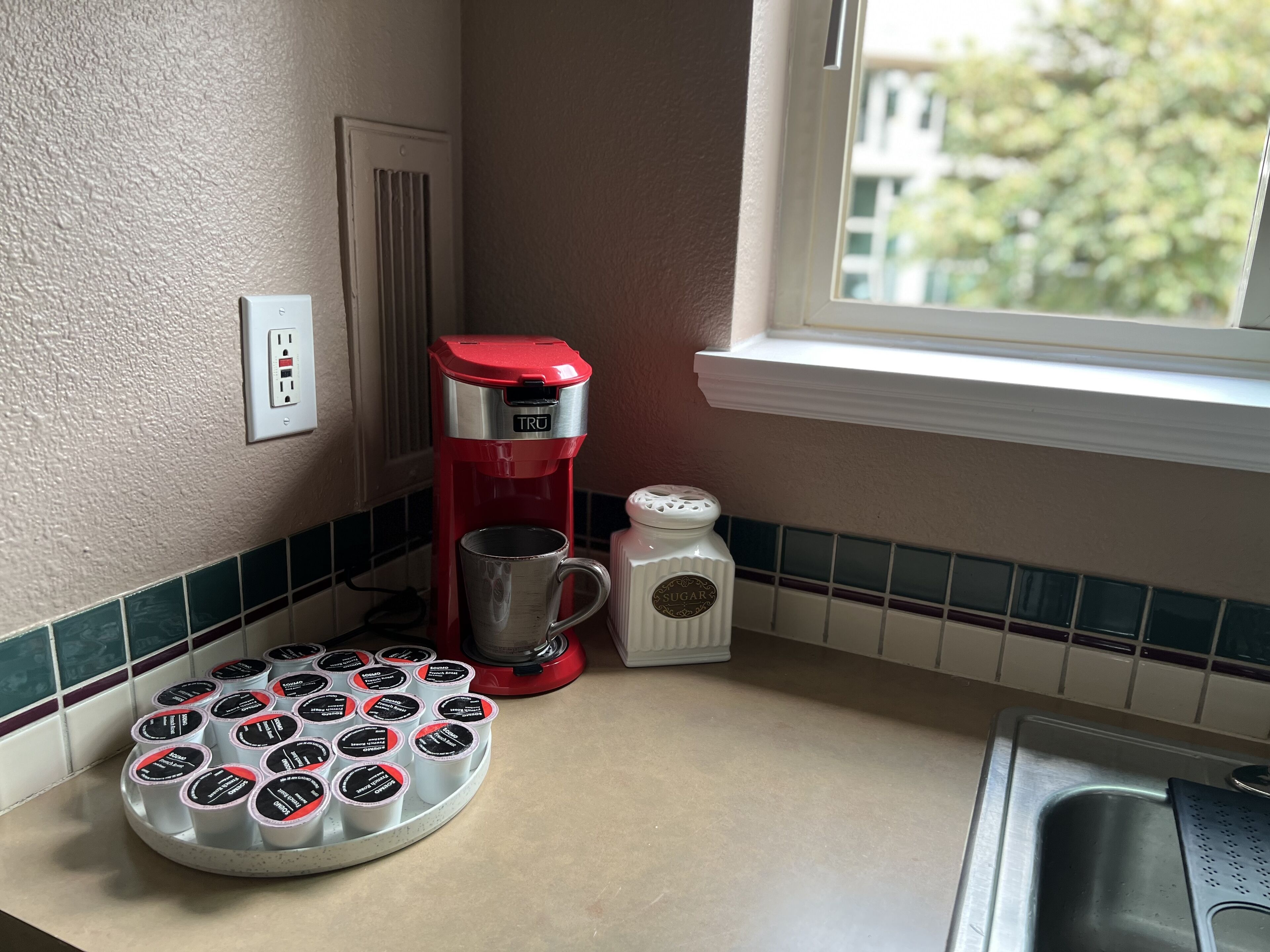 Une cuisine avec une machine à café rouge, un récipient à sucre et un plateau rempli de sachets de sucre.