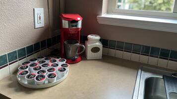 Une cuisine avec une machine à café rouge, un récipient à sucre et un plateau rempli de sachets de sucre.