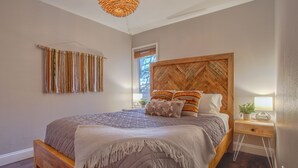 Een slaapkamer met een houten bed, een hoofdeinde met een herringbone-patroon en een nachtkastje met een lamp en een plant.