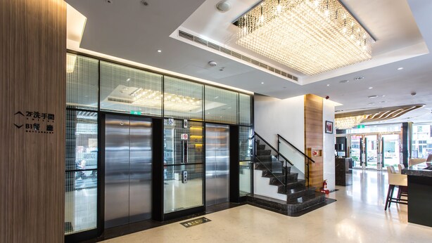A modern hotel lobby with a glass elevator, a staircase, and a chandelier. - Royal Fine Hotel (Kaohsiung)