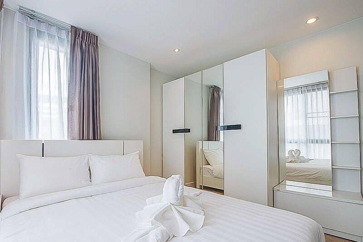 A hotel room with a large bed, a wardrobe, a mirror, and a window with curtains.