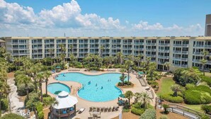 A hotel with a large pool surrounded by palm trees and lounge chairs.