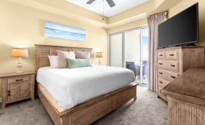 A hotel room with a large bed, a TV, a sliding glass door to a balcony, and a wooden dresser. - The Crescent 412 (Miramar Beach)