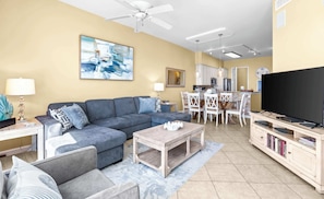 A living room with a sofa, coffee table, TV, and a dining area with chairs and a table.