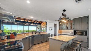 Une cuisine moderne dotée d’un grand îlot central, d’appareils électroménagers intégrés et offrant une vue sur l’extérieur.