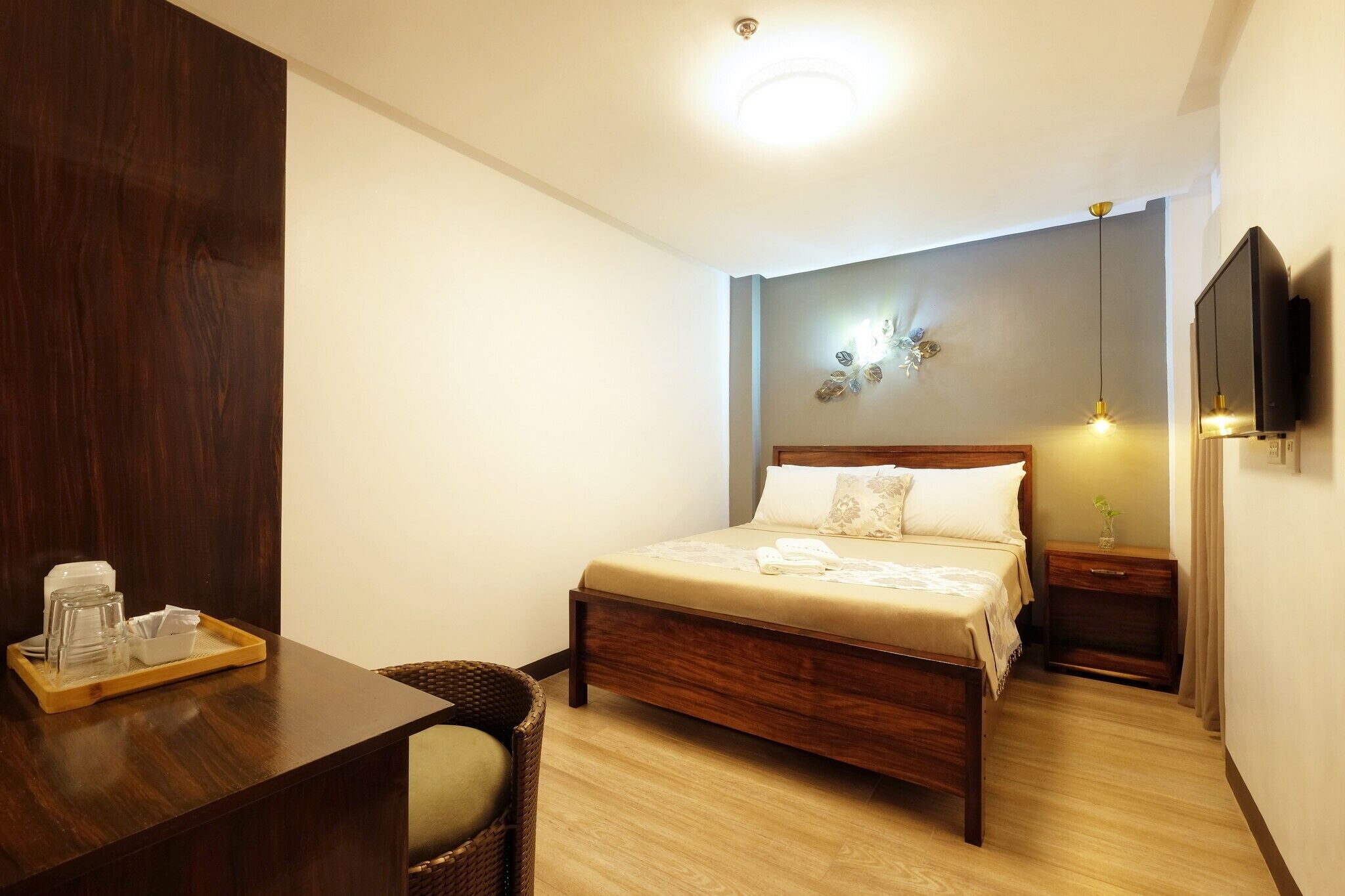 A neatly arranged hotel room with a wooden bed, bedside tables, a TV, and a tray with glasses and a cup.