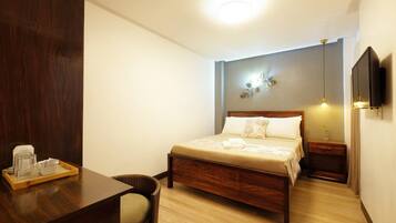 A neatly arranged hotel room with a wooden bed, bedside tables, a TV, and a tray with glasses and a cup.