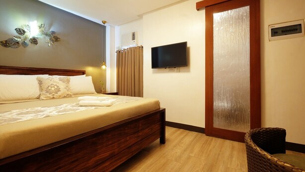 A hotel room with a bed, a television, a wall-mounted air conditioner, and a wicker chair. - Jai-cob's Suites (Coron)