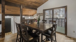 A dining area with a wooden table and chairs, a ceiling fan, and a view of the outside through a large window. - 🏔Family Friendly - Near Airport & Lake w/ Mountain Views - No Chores (Anchorage)
