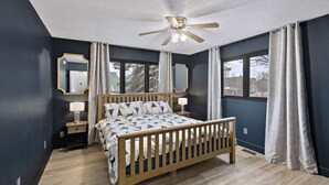A bedroom with a wooden bed, a ceiling fan, a nightstand with a lamp, and a window with curtains. -    🏔Family Friendly - Near Airport & Lake w/ Mountain Views - No Chores (Anchorage)