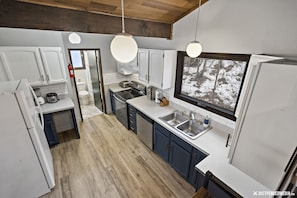 A modern kitchen with white cabinets, a stainless steel sink, and a large window overlooking a snowy landscape.