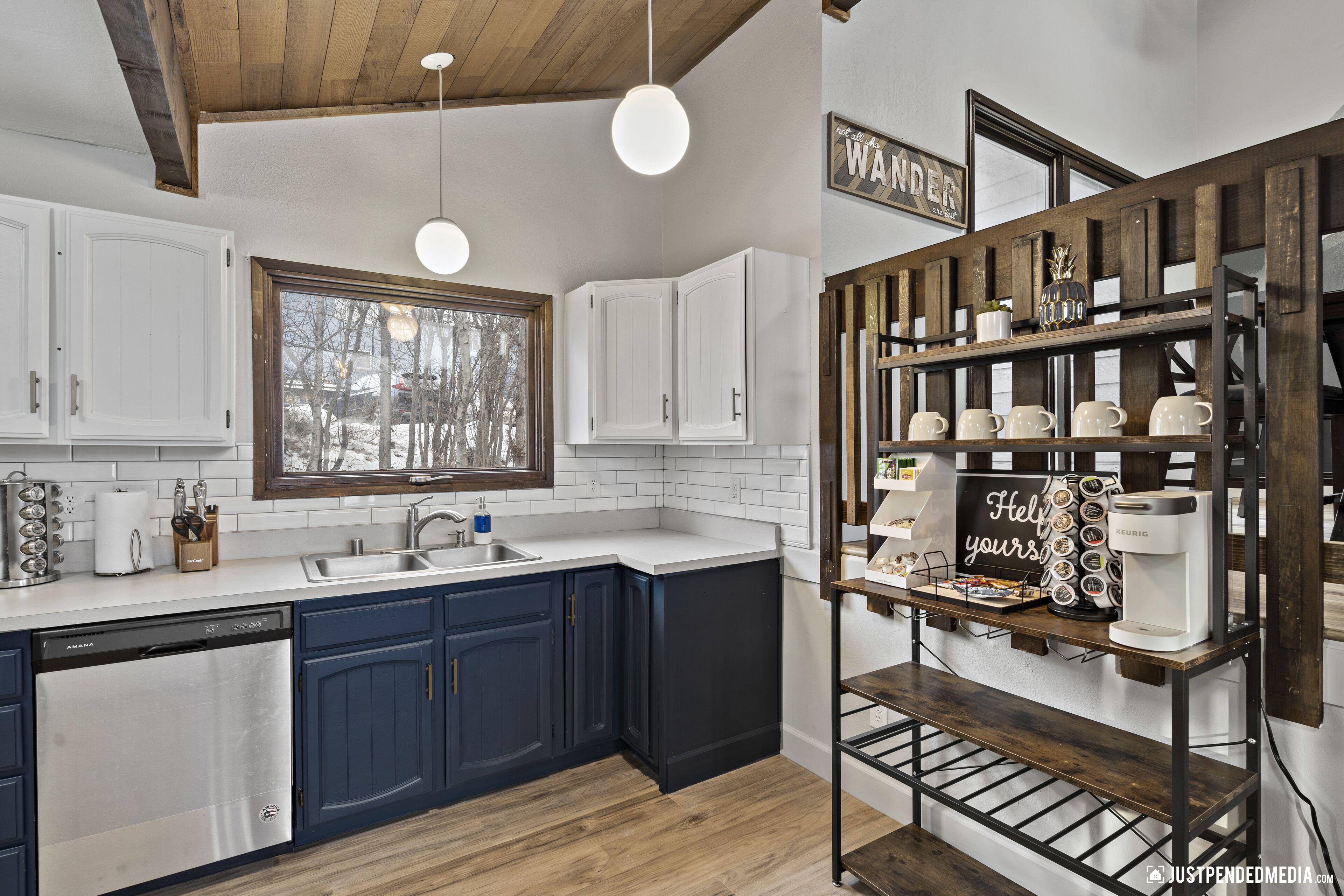 Una cocina moderna con armarios blancos y azul oscuro, lavavajillas integrado, encimera de madera y cafetera.