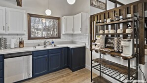 A modern kitchen with white and dark blue cabinets, a built-in dishwasher, a wooden countertop, and a coffee machine. - 🏔Family Friendly - Near Airport & Lake w/ Mountain Views - No Chores (Anchorage)