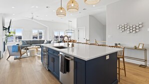 Une cuisine moderne dotée d’un grand îlot central, de planchers en bois et de luminaires suspendus.