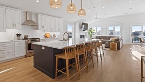 Une cuisine spacieuse dotée d’un grand îlot central, de meubles blancs et d’une cuisinière moderne.