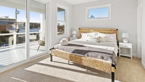 Une chambre avec un grand lit, un banc en osier, une table de chevet et une vue sur l’extérieur.