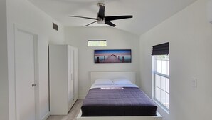 Une chambre à coucher avec un lit, un ventilateur de plafond, une fenêtre et un tableau accroché au mur.