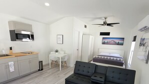Une chambre moderne avec un lit, un canapé noir, une petite table et un coin cuisine.