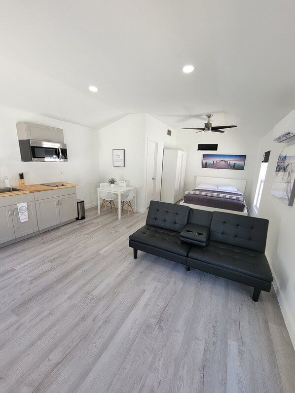 A modern bedroom with a bed, a black sofa, a small table, and a kitchenette.